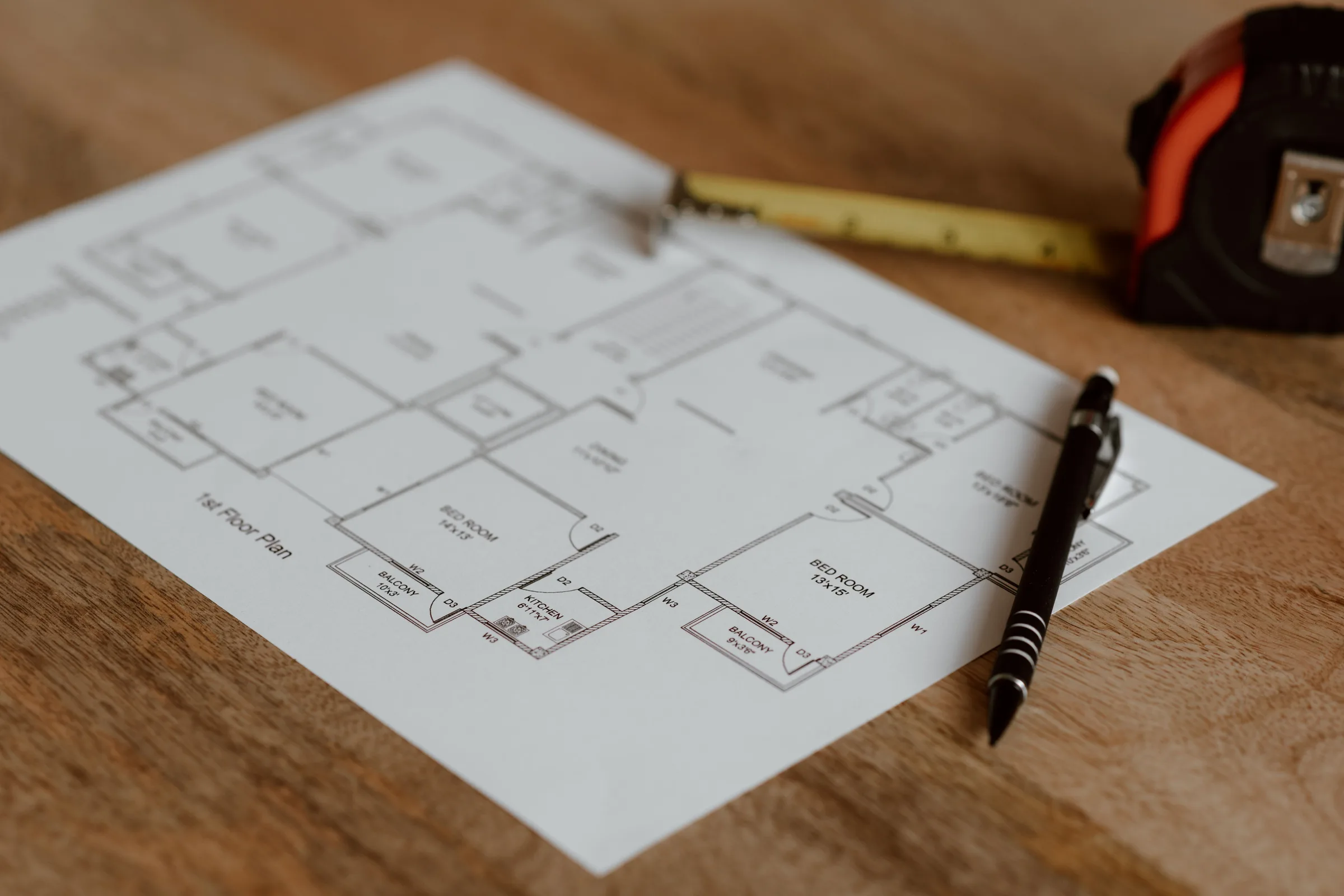 A floor plan on a wooden desk with a pencil and a tape measure