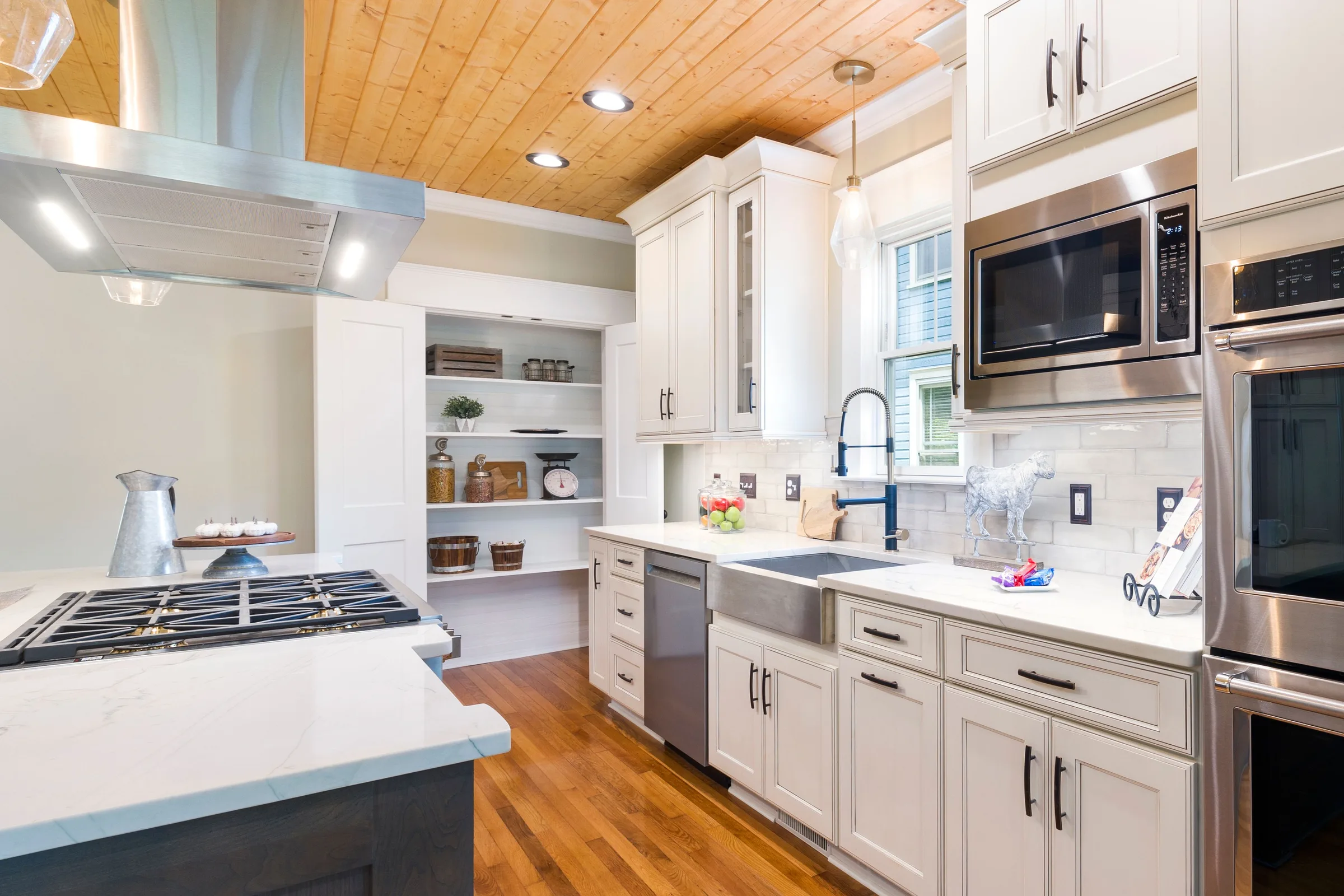 A finished kitchen with a planked wood ceiling, cream cabinets, a dark island and a range hood