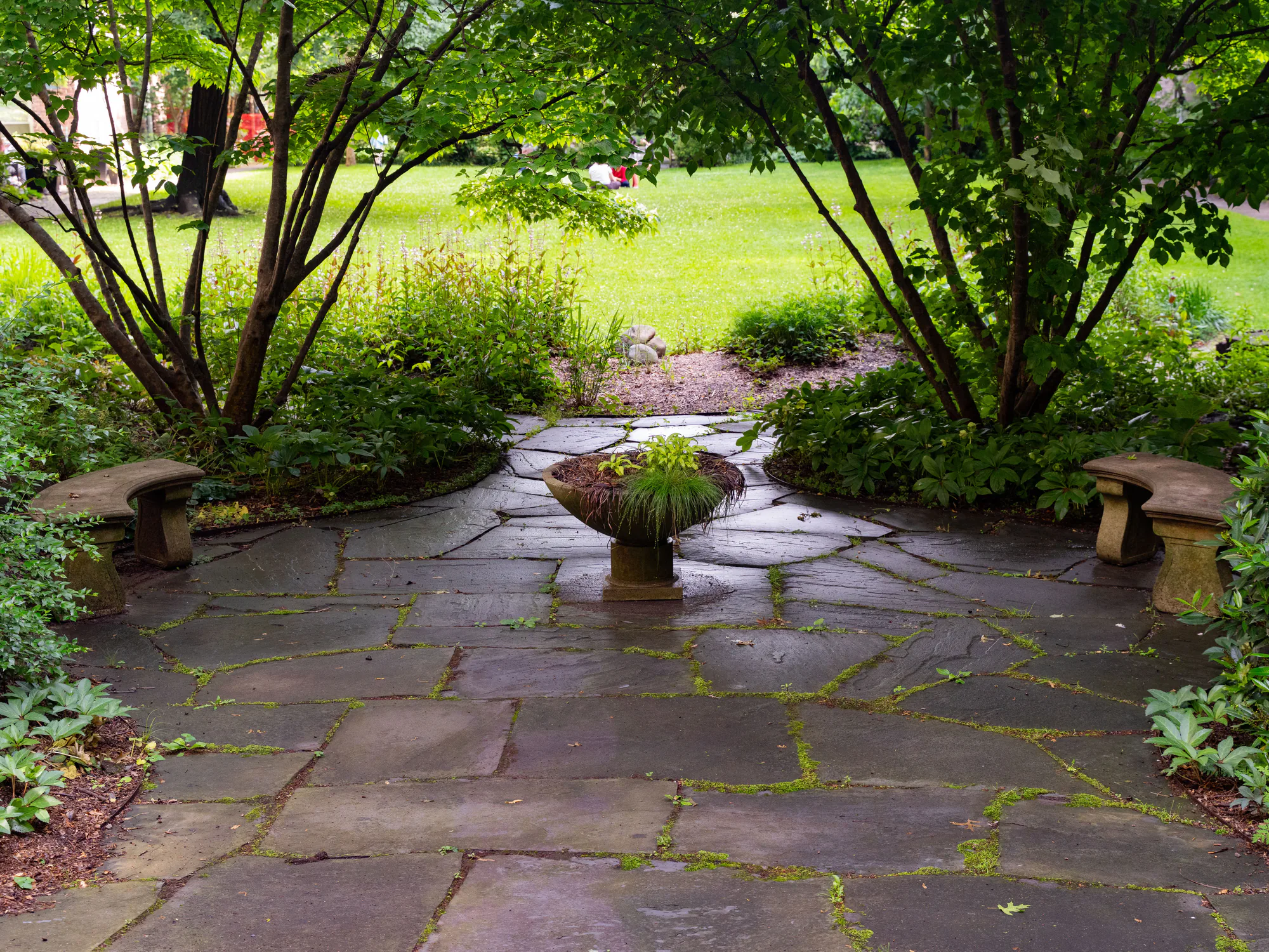 A flagstone patio with a stone planter, ringed by garden trees