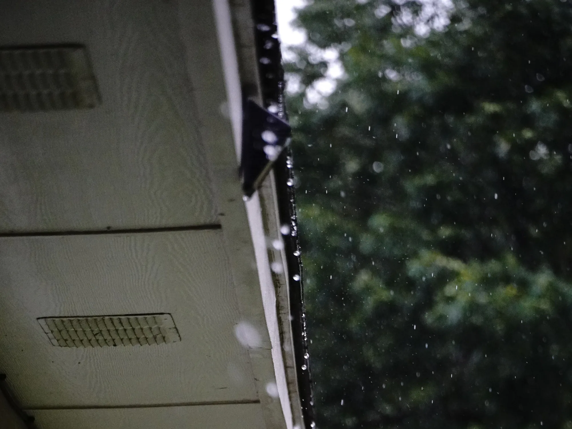 Vents in a painted soffit under a roof edge, rain falling past