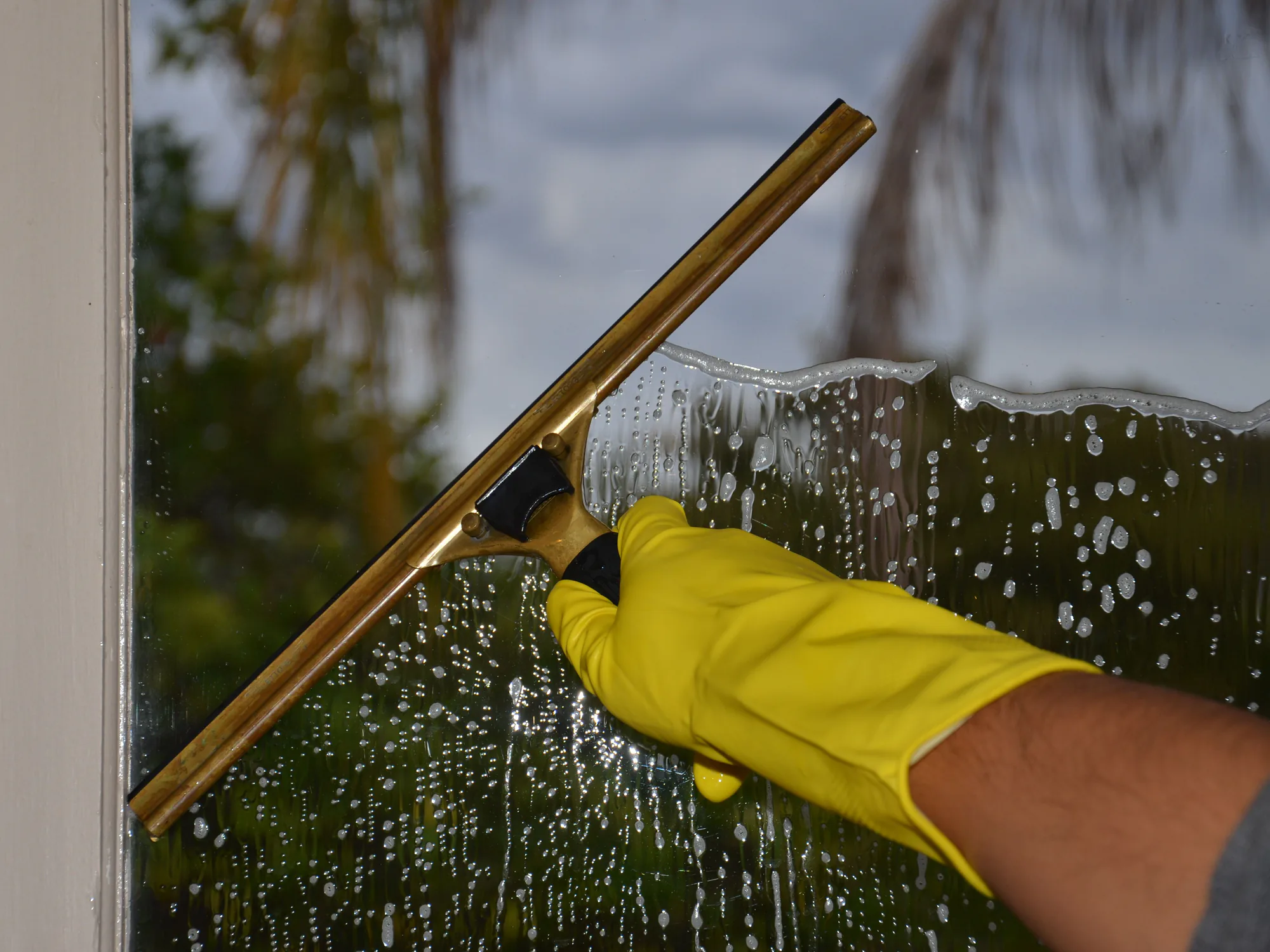 A yellow-gloved hand drawing a squeegee across a soapy window