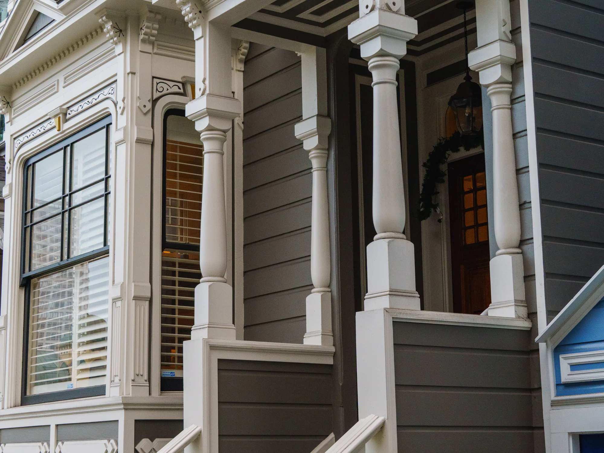 A Victorian porch with turned white columns and grey painted siding