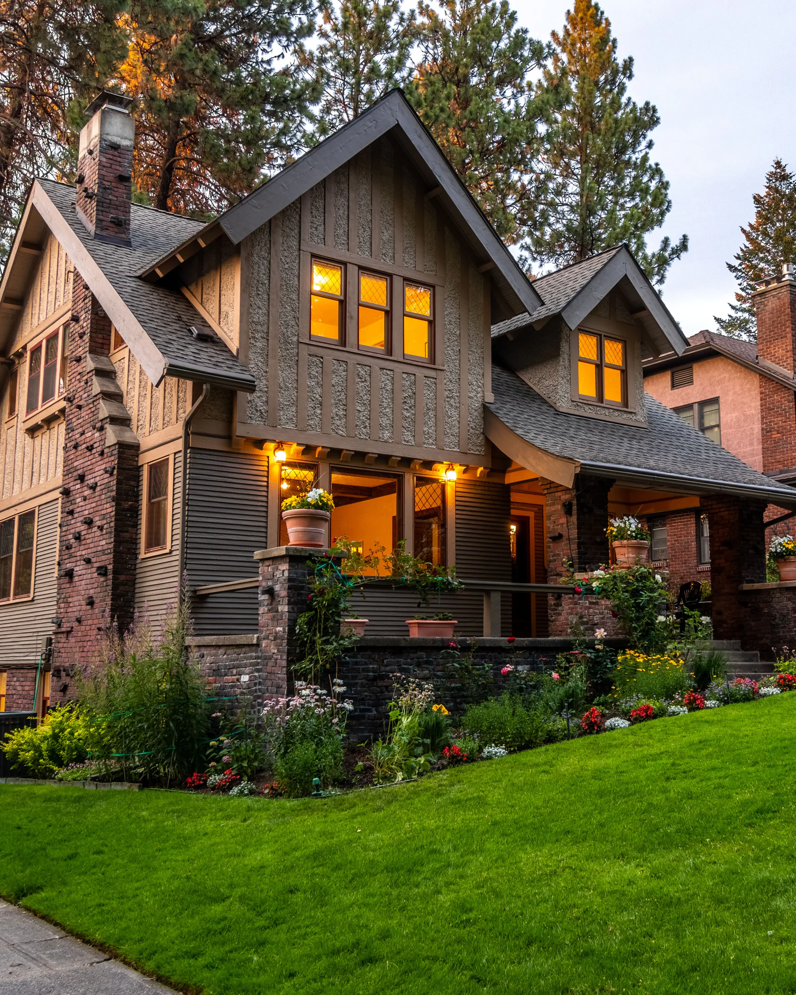 A Craftsman house with lit windows at dusk above a green lawn