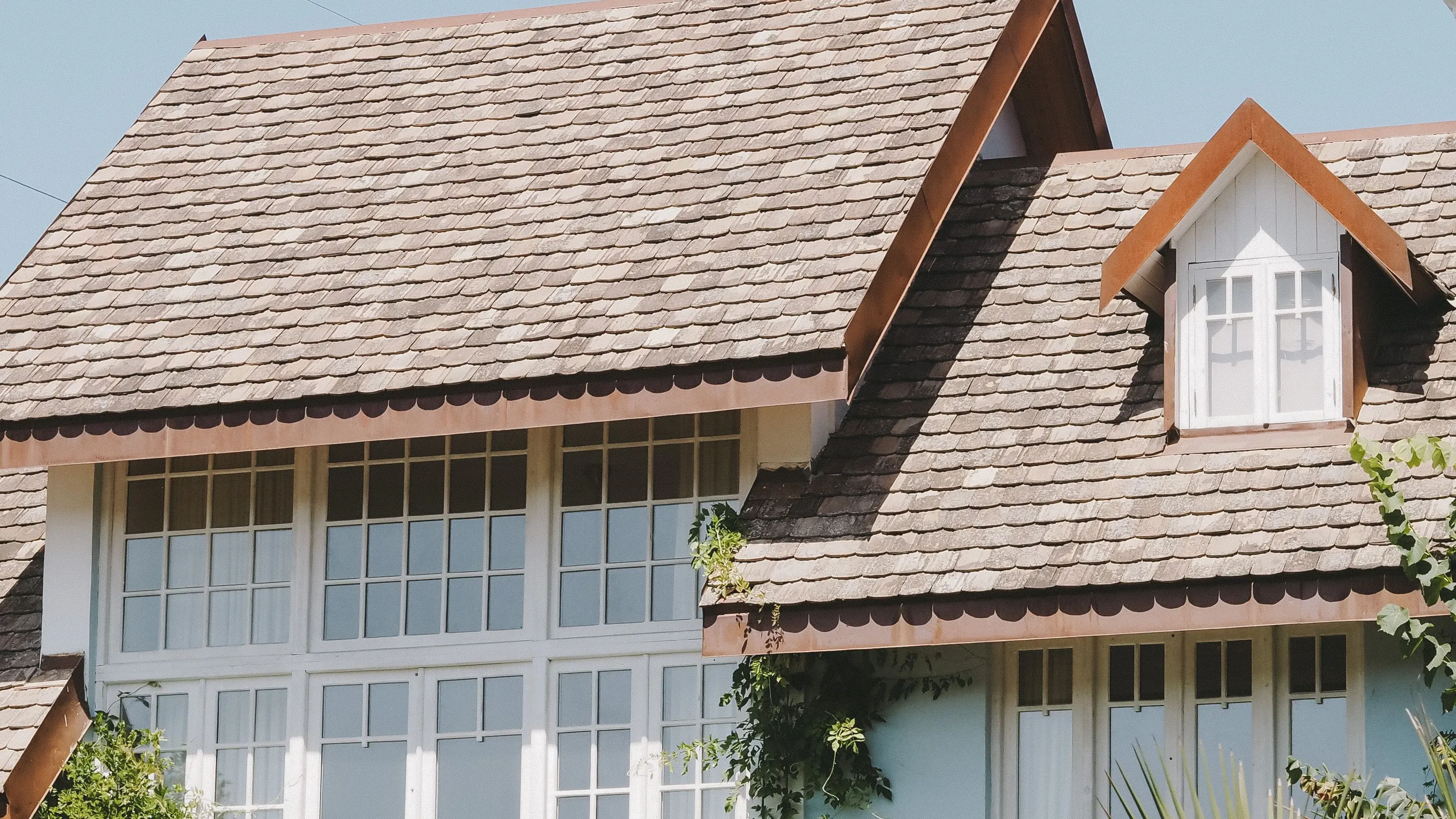 A pale blue house with a wood shingle roof, a small dormer and tall white paned windows