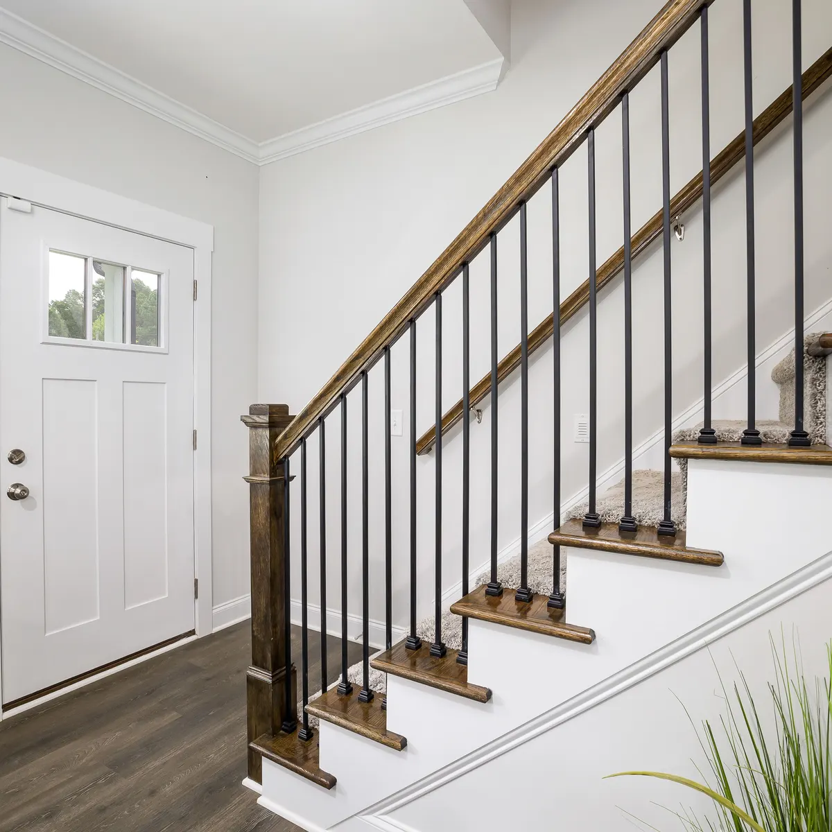 A white front door, baseboards and a staircase with dark wood treads and iron balusters