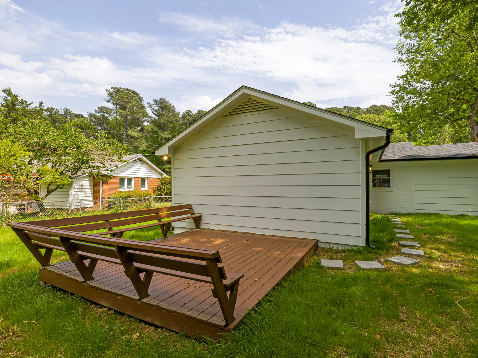 A stained wooden deck with built-in benches beside a pale sided outbuilding