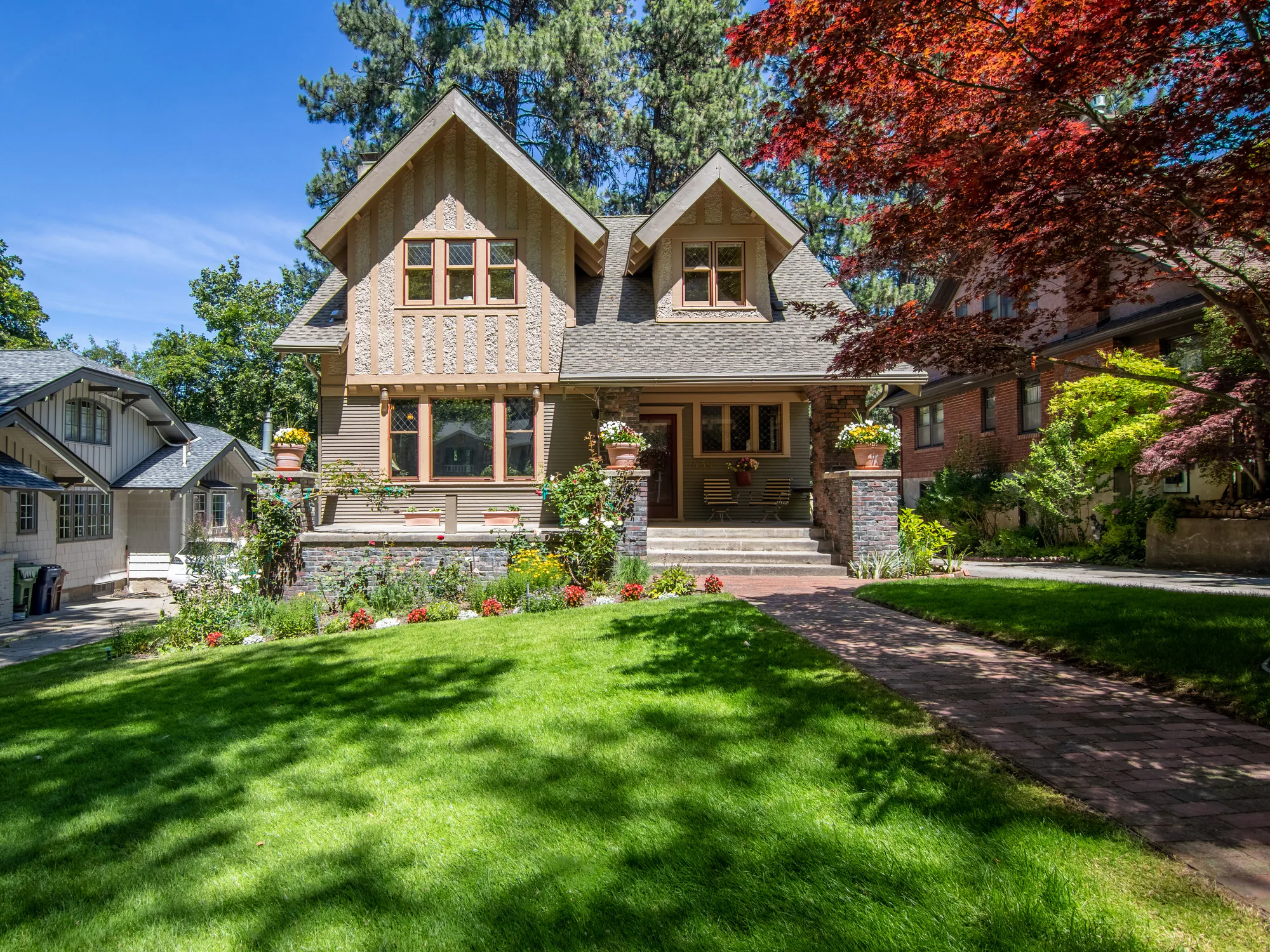 A tan Craftsman house with a sunlit front lawn and flower beds