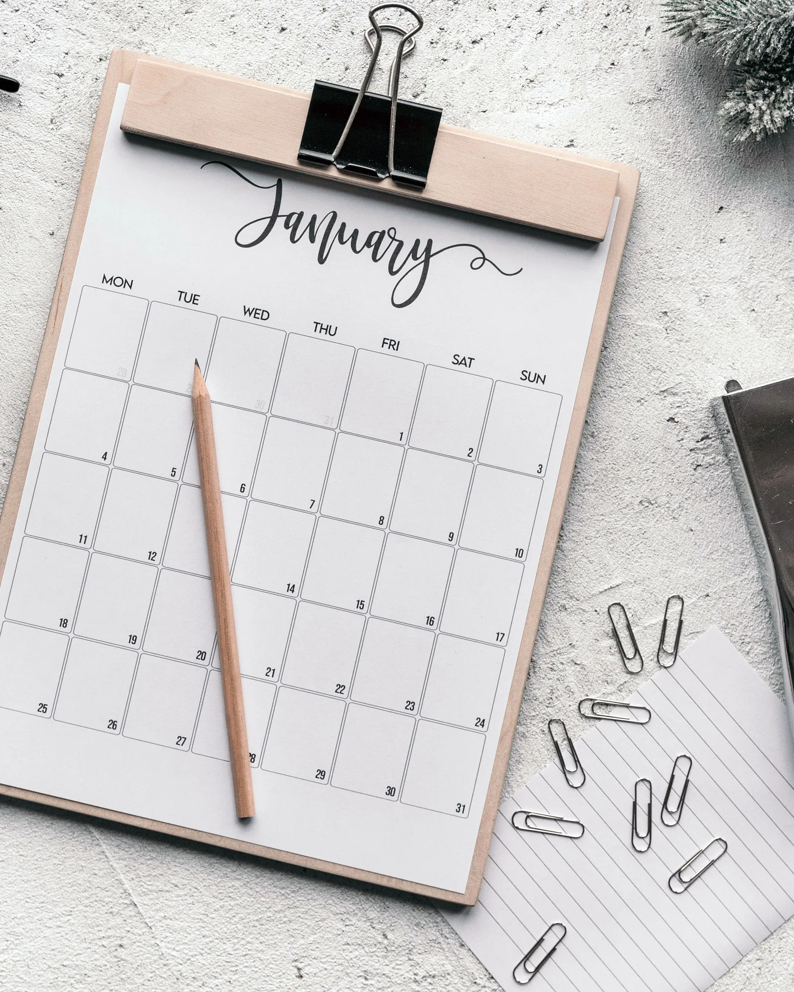 A calendar on a clipboard beside a pencil and paper clips