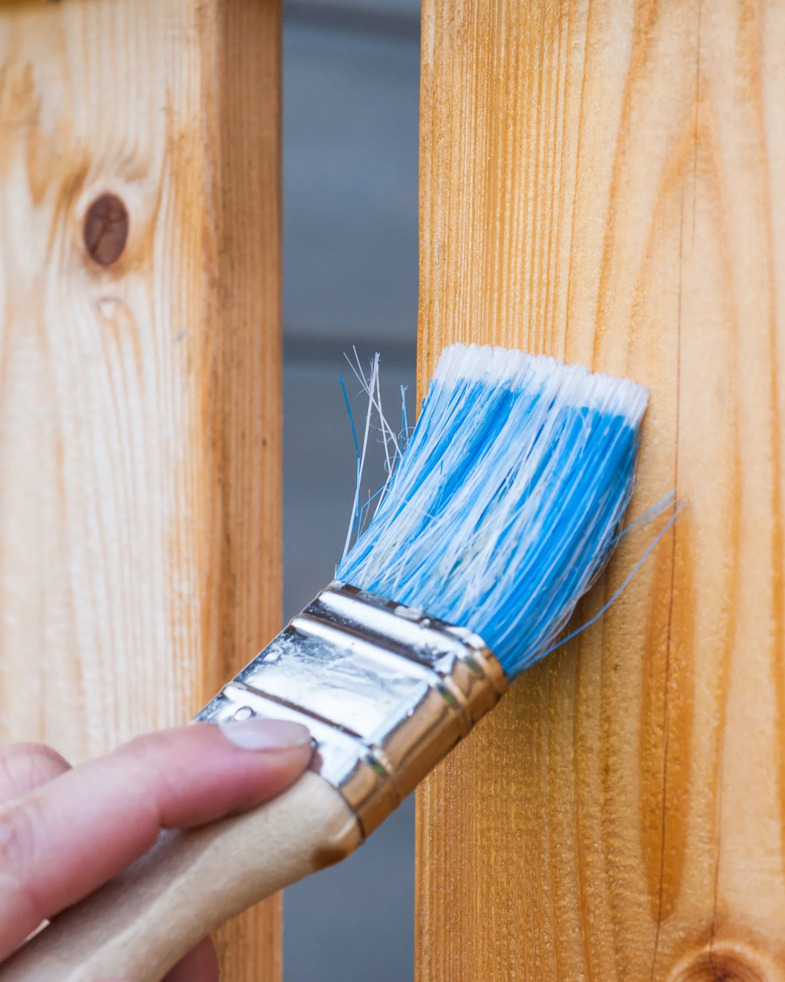 A hand brushing paint onto a wooden fence board