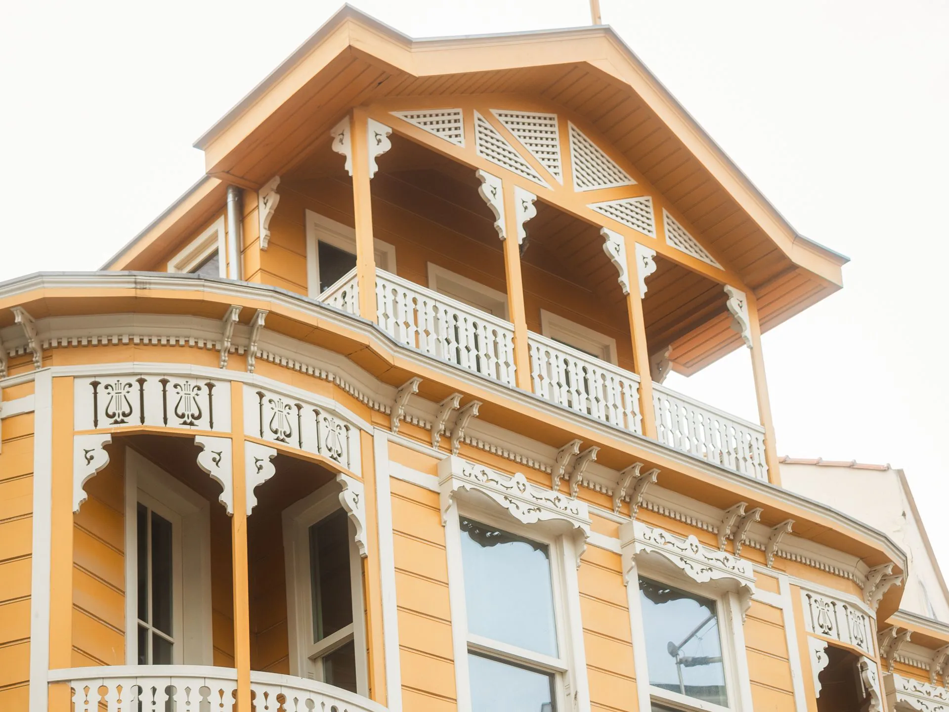 A yellow Victorian house with white fretwork balconies and trim