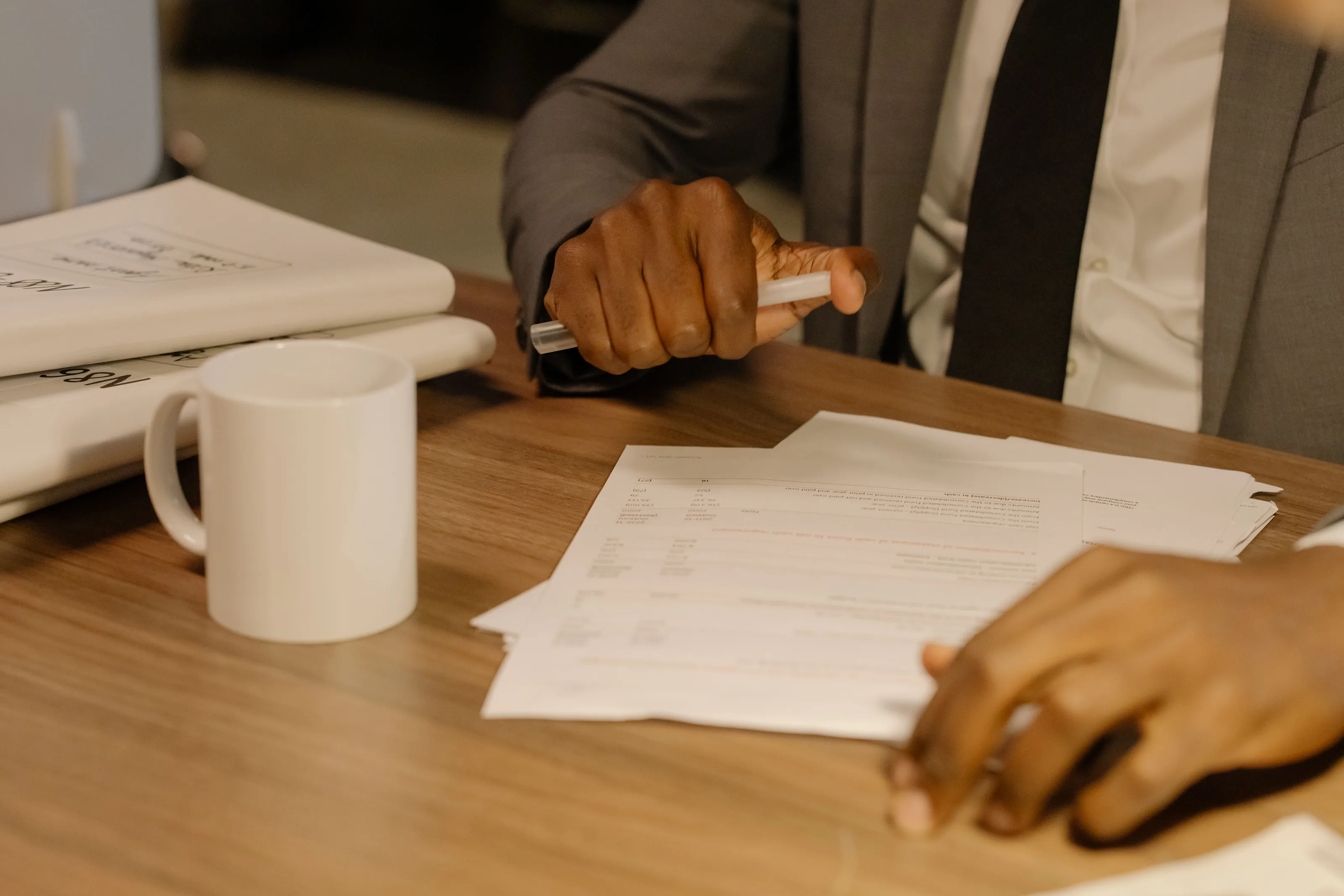 Hands over printed pages on a wooden desk beside a white mug