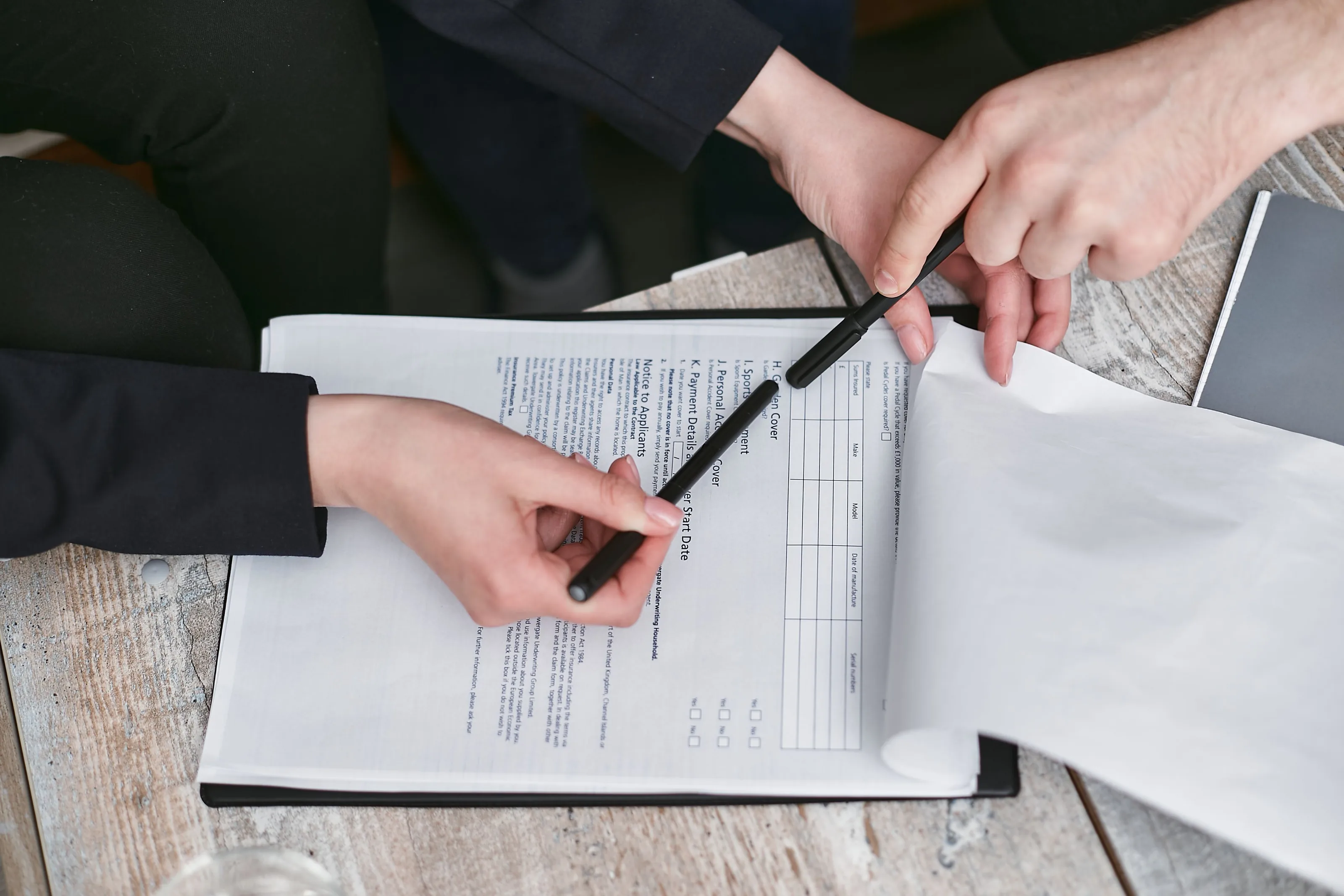 One hand passing a pen to another over a printed form on a clipboard