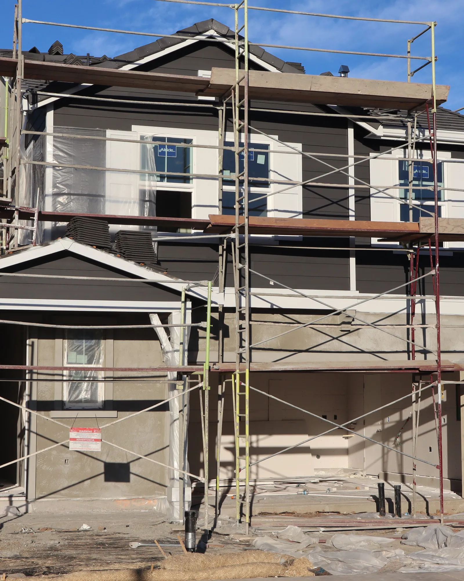 A two-story house wrapped in scaffolding under a clear blue sky