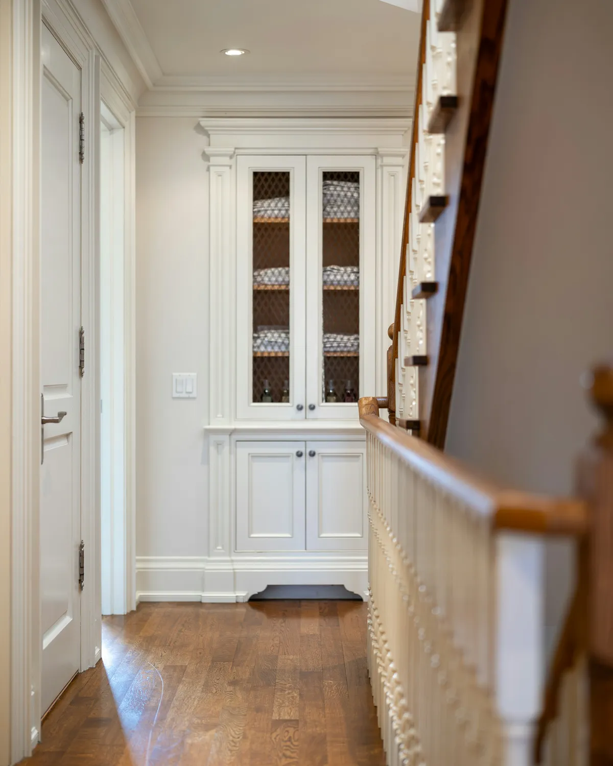 A built-in glass-front cabinet at the end of a hallway, with paneled trim and a stair railing