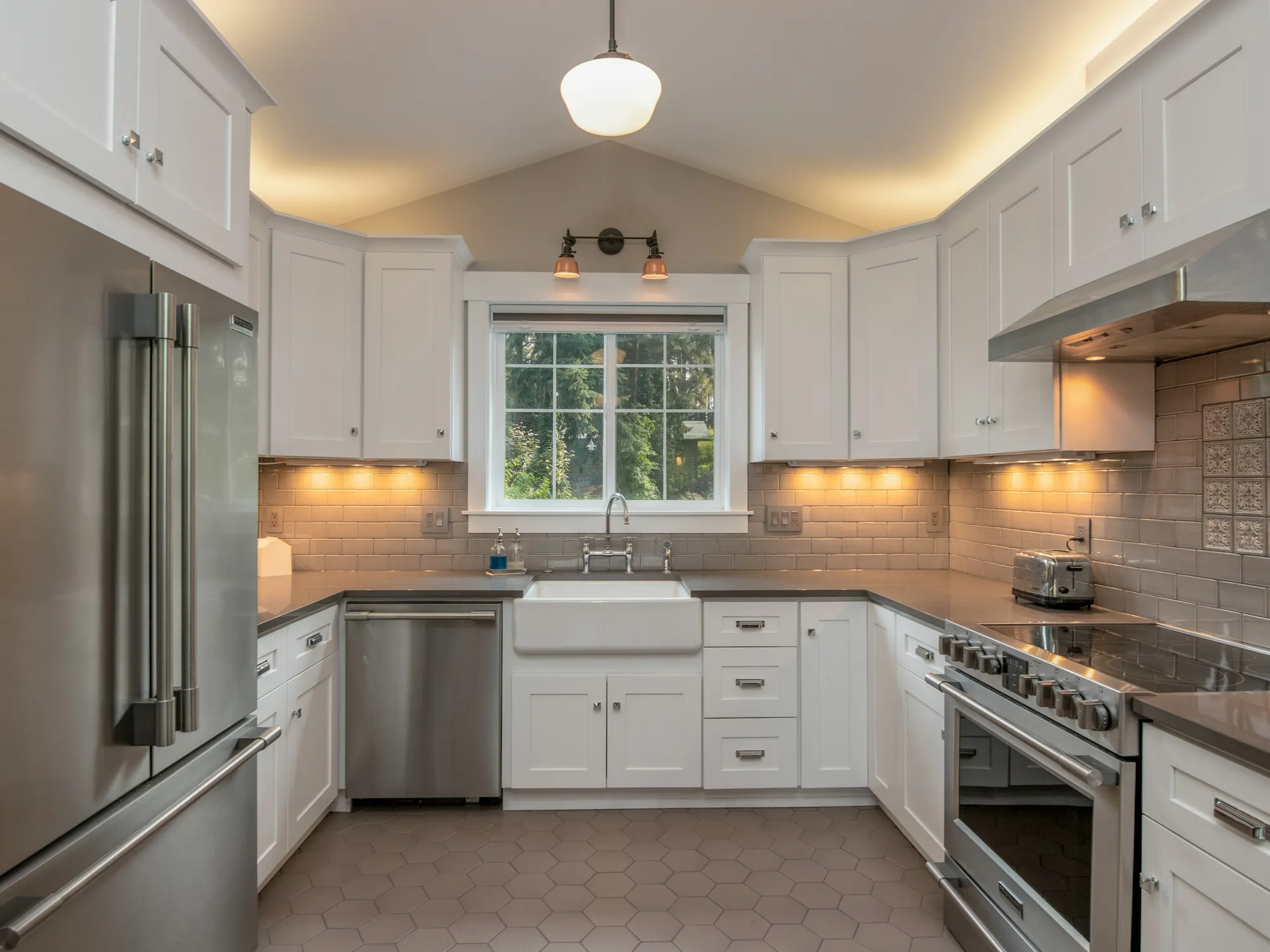 A white kitchen with shaker cabinets, a farmhouse sink under the window and under-cabinet lighting