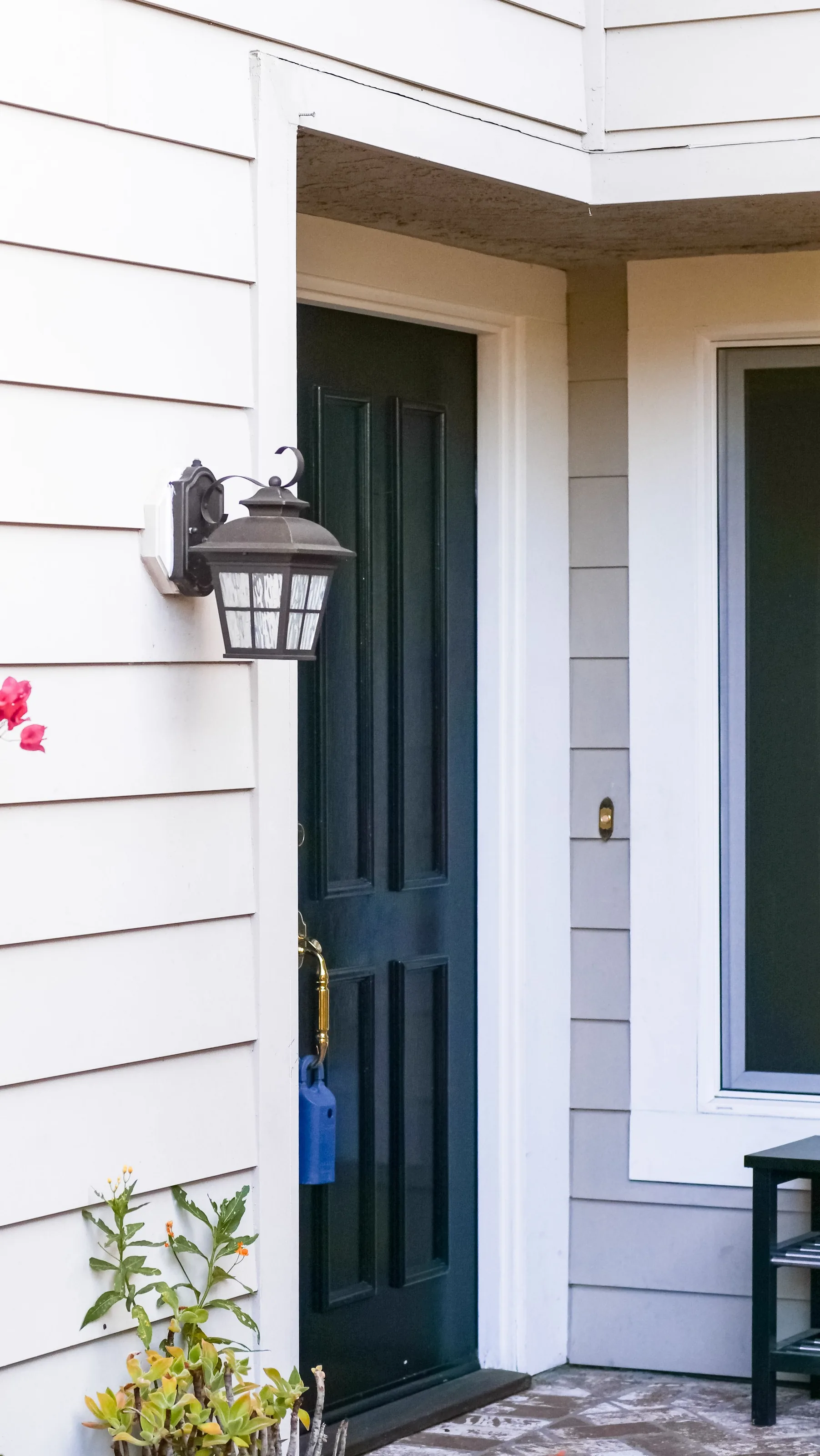 A dark green high-gloss front door with a brass knob and a black lantern sconce on white clapboard siding