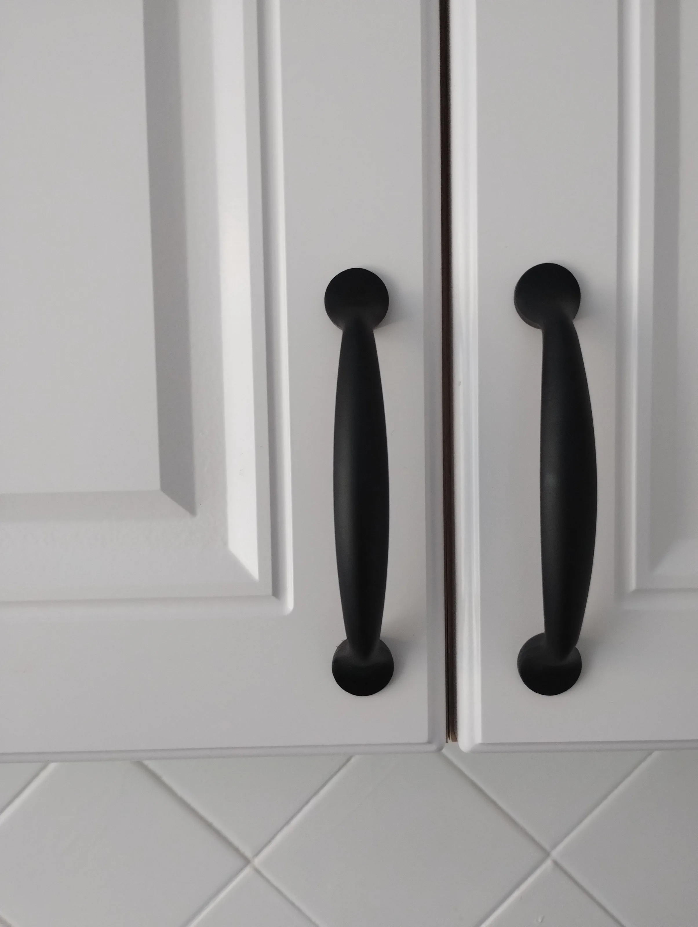 Two white painted cabinet doors with matte black pulls, close up