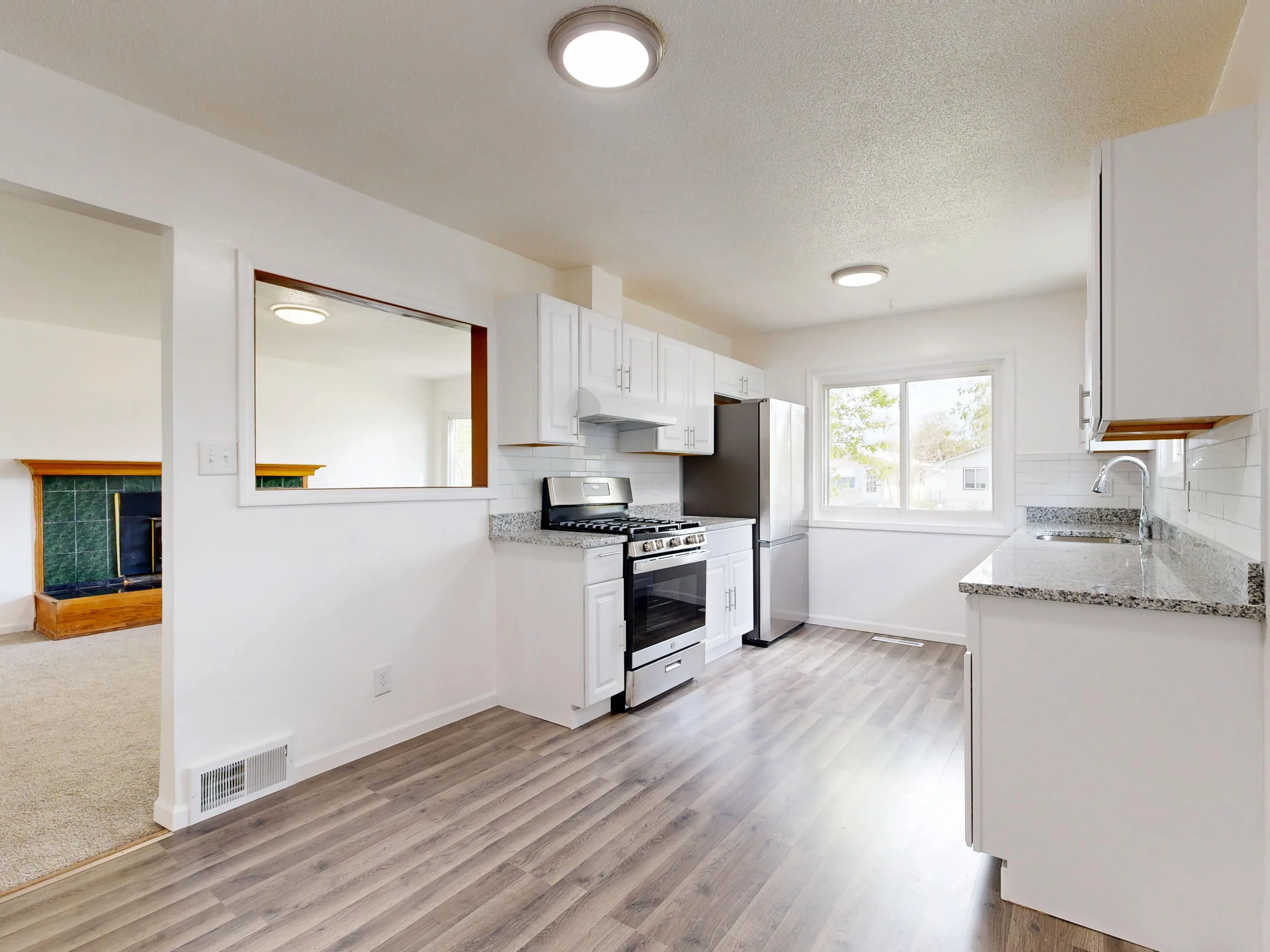 A renovated kitchen with white cabinets, a granite counter and hardwood floors