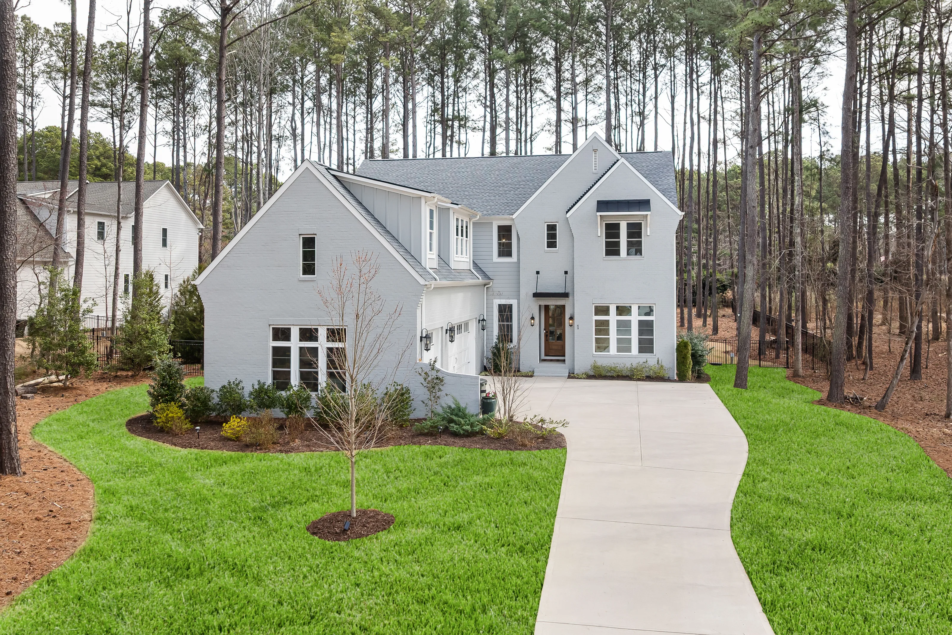 A two-story house with pale grey lap siding on a lawn among tall pines