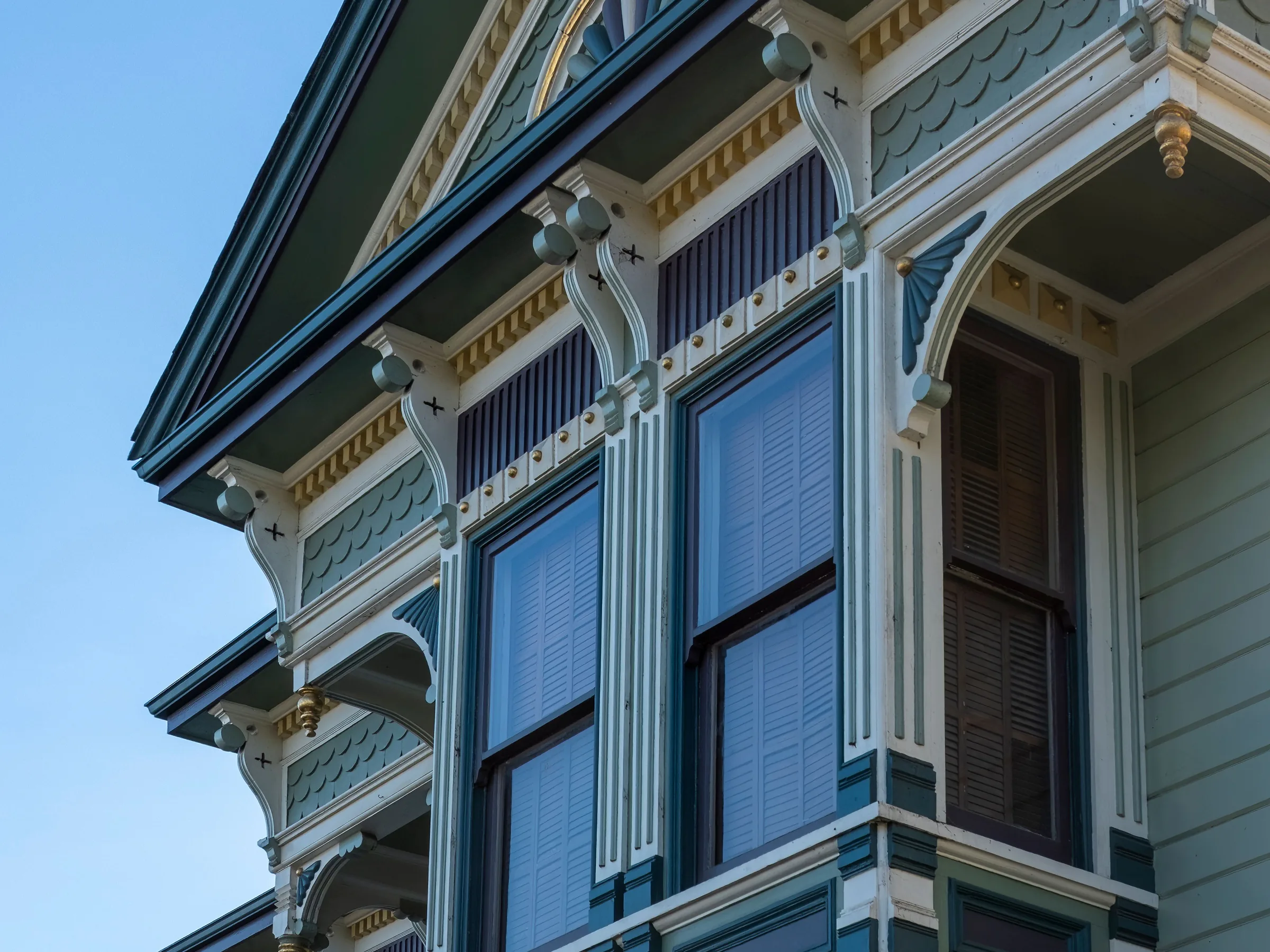 A Victorian bay window with ornate brackets and dentil trim painted navy, sage, cream and gold