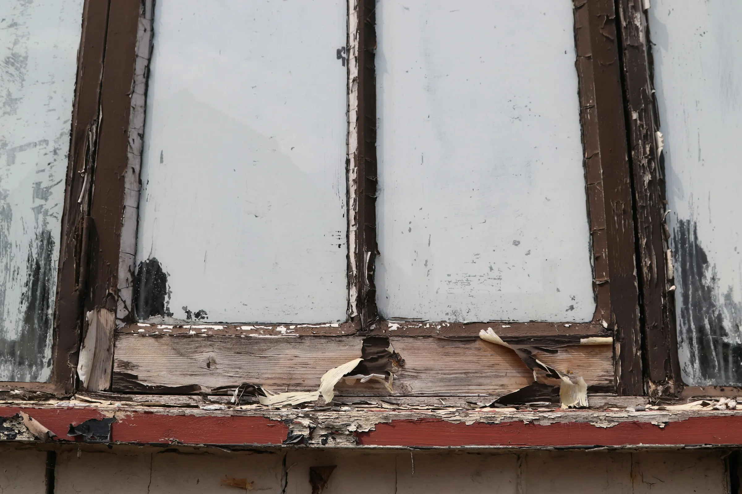 A decayed wooden window frame with its sill split and paint peeling off the wood