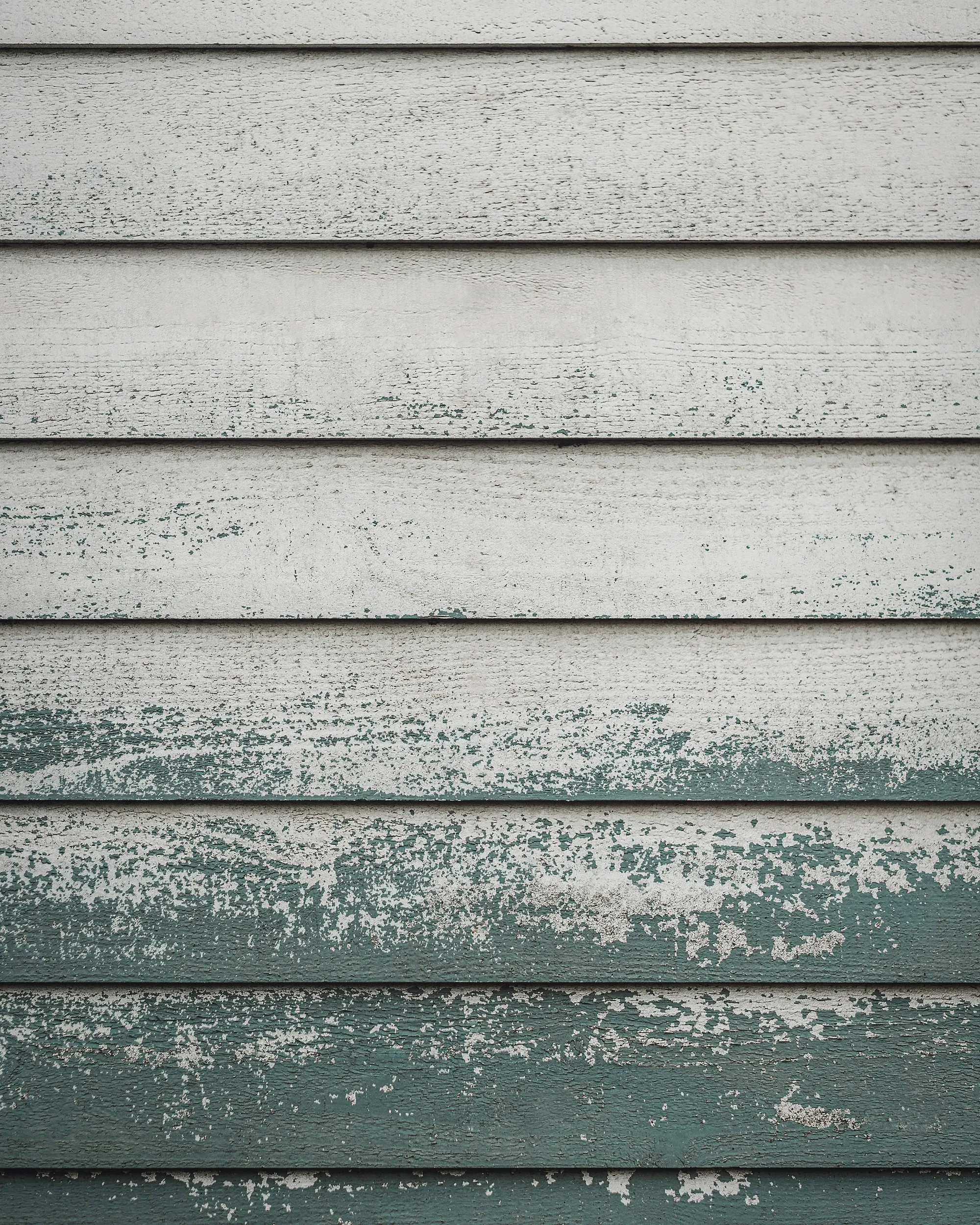 Horizontal wood siding with its white and green paint weathered and peeling