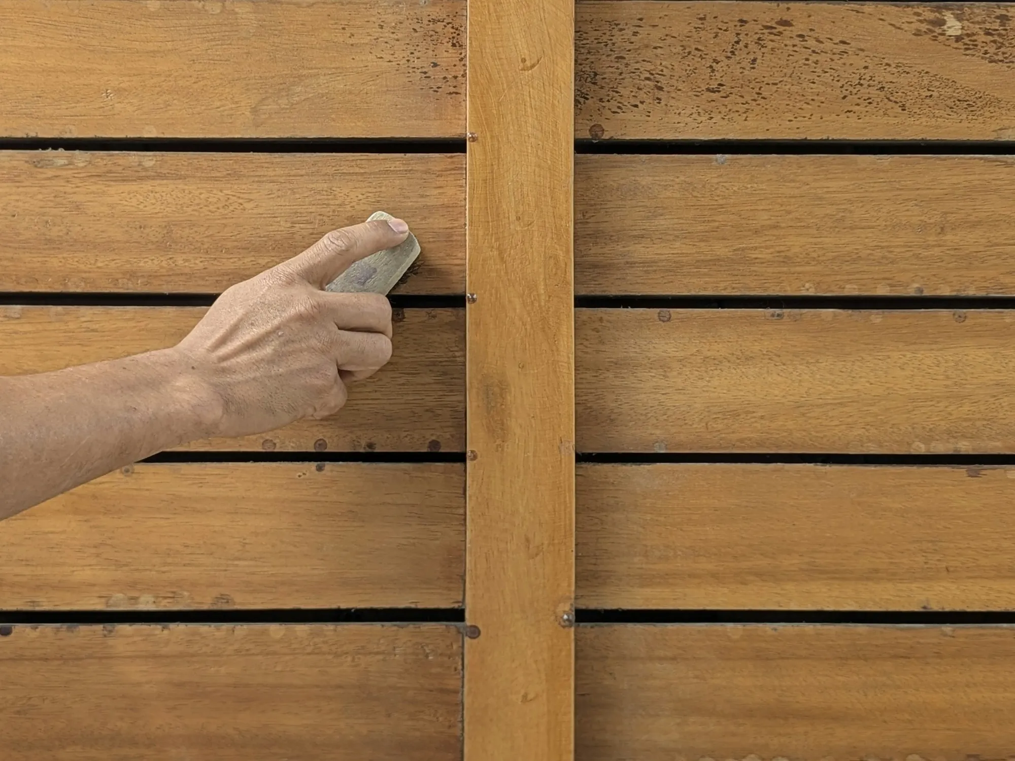 A hand sanding a horizontal wood board with a sanding block