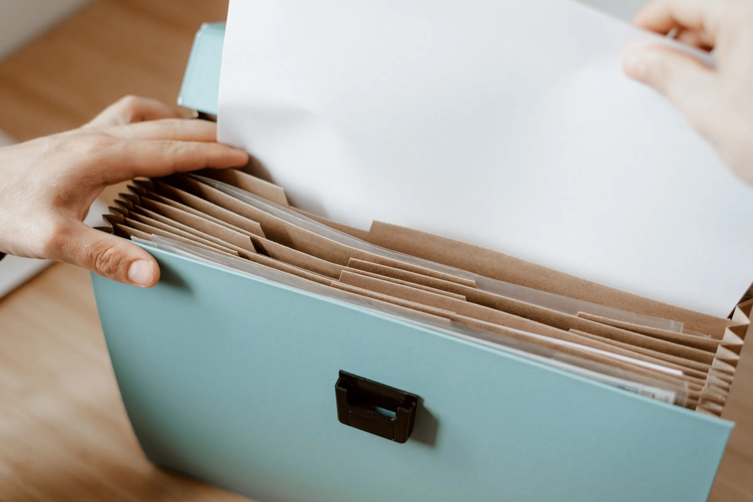 Two hands slip a sheet of paper into an expanding file folder on a wooden table