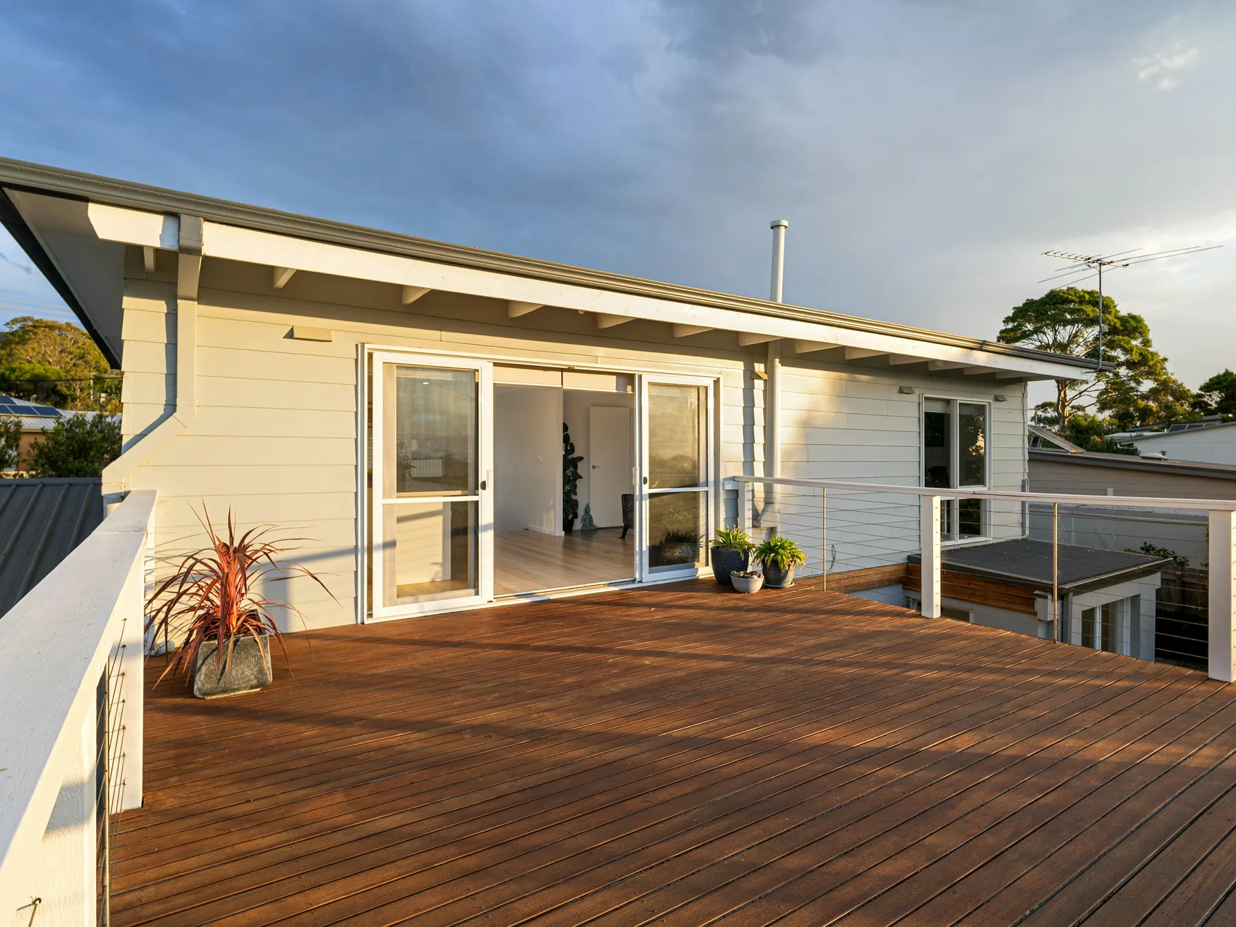 A hardwood deck running up to a white clapboard house with glass doors and a cable railing